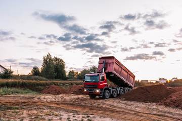 A dump truck is dumping gravel on an excavation site