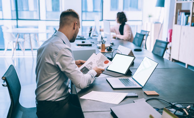 Focused man browsing laptop in office and studying papers