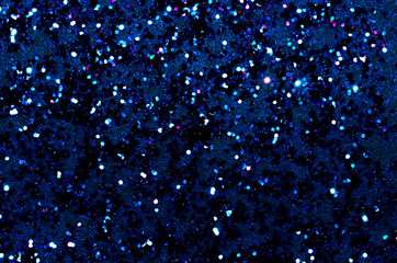 Texture of multicolor glitter spangles on a dark blue background with space for text.
