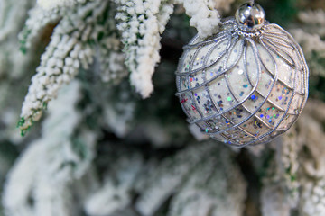 Close up of beautiful christmas decoration- bauble silver ball hanging on the Christmas tree on the background of snow-covered branches. Silver beige Christmas winter background