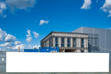 Blank white banner for advertisement on the fence of factory under construction. Industrial area on a sunny day © diesirae