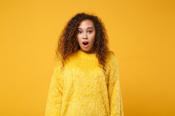 Shocked excited young african american girl in fur sweater posing isolated on yellow orange background in studio. People sincere emotions lifestyle concept. Mock up copy space. Keeping mouth open.