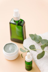 beauty, spa and wellness concept - serum, clay mask, oil and eucalyptus cinerea on bath towel
