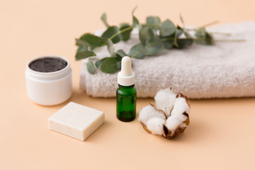 Obraz na płótnie Canvas beauty and spa concept - serum or essential oil, mask, soap bar, eucalyptus cinerea and cotton flower on bath towel