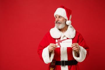 Smiling elderly gray-haired mustache bearded Santa man in Christmas hat isolated on red wall background. Happy New Year 2020 celebration holiday concept. Mock up copy space. Holding gift certificate.