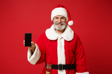 Fototapeta na wymiar Smiling elderly gray-haired mustache bearded Santa man in Christmas hat isolated on red background. New Year 2020 celebration holiday concept. Mock up copy space. Hold mobile phone with blank screen.