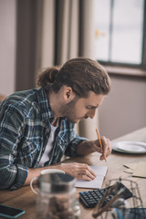 Young long-haired man writing on the piece of paper