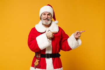 Fototapeta na wymiar Funny elderly gray-haired bearded mustache Santa man in Christmas hat posing isolated on yellow background. New Year 2020 celebration holiday concept. Mock up copy space. Pointing index fingers aside.