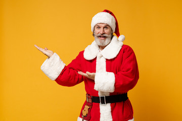 Fototapeta na wymiar Smiling elderly gray-haired bearded mustache Santa man in Christmas hat posing isolated on yellow background. Happy New Year 2020 celebration holiday concept. Mock up copy space. Pointing hands aside.