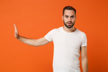 Young man in casual white t-shirt posing isolated on bright orange wall background studio portrait....
