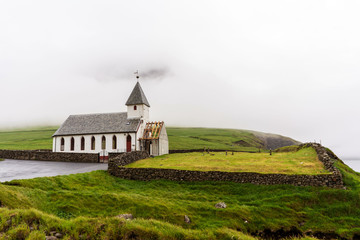 Traditional Faroese wooden church surrounded with green hills, overcast sky on horizon. Faroe Islands, Denmark.