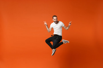 Fototapeta na wymiar Funny young man in casual white t-shirt posing isolated on orange background studio portrait. People sincere emotions lifestyle concept. Mock up copy space. Having fun jumping, showing victory sign.