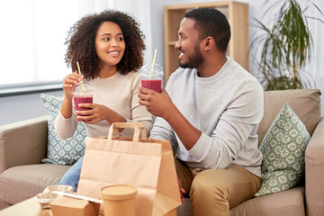 eating and people concept - happy african american couple with takeaway food and drinks at home