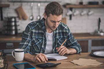 Thoughtful long-haired man writing his ideas into a notebook.