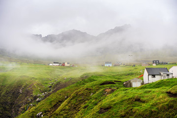 Foggy morning in Vidareidi village with white wooden houses surrounded with green hills. Faroe Islands, Denmark.