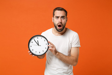 Shocked young man in casual white t-shirt posing isolated on bright orange wall background studio...