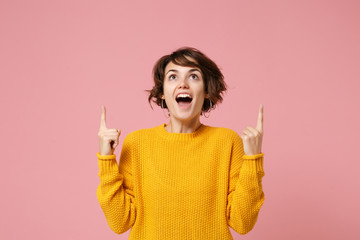 Amazed young brunette woman girl in yellow sweater posing isolated on pastel pink background,...