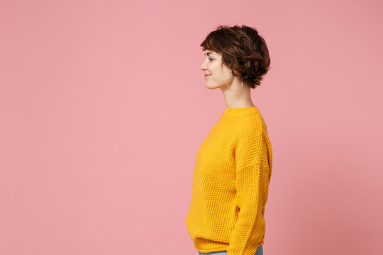 Side view of smiling young brunette woman girl in yellow sweater posing isolated on pink wall background, studio portrait. People sincere emotions lifestyle concept. Mock up copy space. Looking aside.