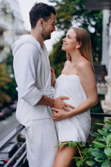 Naklejka premium Pregnant woman wrapped in towel on balcony with husband