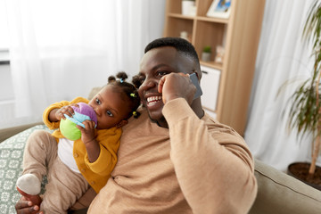 family, fatherhood and technology concept - happy african american father with baby at home calling...