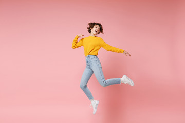 Fototapeta na wymiar Funny young brunette woman girl in yellow sweater posing isolated on pastel pink background in studio. People lifestyle concept. Mock up copy space. Having fun fooling around, looking aside, jumping.