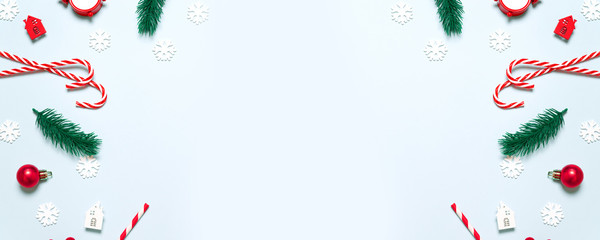 Flat lay spruce twigs, christmas balls, candy cane, house and star on a minimal blue background