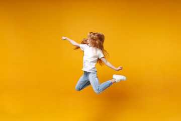 Fototapeta na wymiar Side view of little ginger kid girl 12-13 years old in white t-shirt isolated on yellow background children portrait. Childhood lifestyle concept. Mock up copy space. Having fun, fooling around, jump.