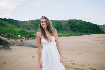 Fototapeta na wymiar Pretty cheerful woman in white dress walking along beach