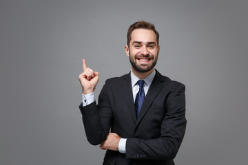 Smiling young bearded business man in classic black suit shirt tie posing isolated on grey wall...