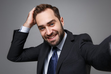 Close up of young business man in suit shirt tie posing isolated on grey background. Achievement career wealth business concept. Mock up copy space. Doing selfie shot on mobile phone put hand on head.