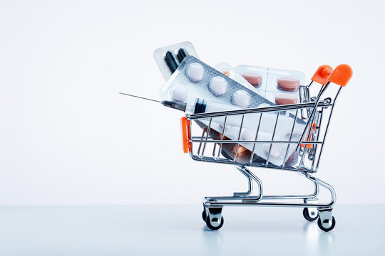 Medical pills in blister packs and a syringe in a shopping cart on white background