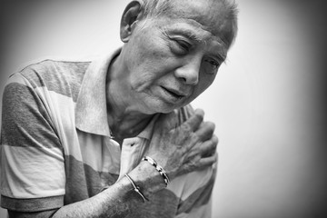 Fototapeta na wymiar Elderly Asian man put his hand on his shoulder because of shoulder pain or muscle pain. Healthcare and Medical concept. Black and white tone