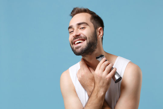 Close Up Bearded Young Man 20s Years Old In White Shirt Hold Electric Razor Isolated On Blue Pastel Background, Studio Portrait. Skin Care Healthcare Cosmetic Procedures Concept. Mock Up Copy Space.