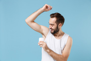 Bearded young man 20s years old in white shirt hold using antiperspirant isolated on blue pastel...