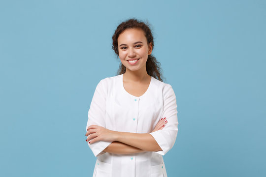 Pretty African American Doctor Woman Isolated On Blue Background In Studio. Female Doctor In White Medical Gown Holding Hands Crossed. Healthcare Personnel Health Medicine Concept. Mock Up Copy Space.