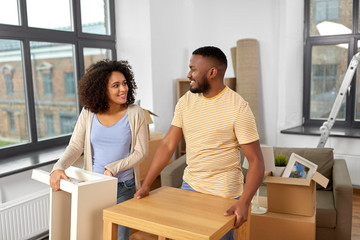 moving, people, repair and real estate concept - happy african american couple with tables stuff at...