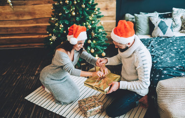 Couple opening Christmas presents in decorated bedroom