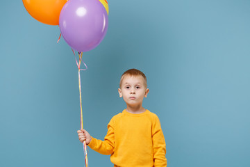 Little cute kid boy 4-5 years old have fun celebrating birthday holiday party with colorful air balloons isolated on pastel blue wall background. People sincere emotions, childhood lifestyle concept.