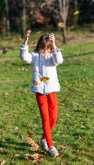 Little girl in autumn park. Girl playing with leaves