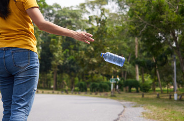 Hands of yellow shirt woman throwing empty plastic bottle in the park. Do not waste the garbage concept.