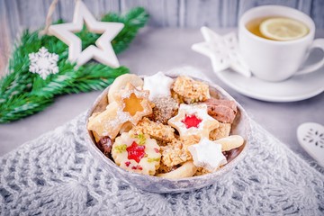 Homemade assorted cookies in ceramic bowl, tea, christmas tree branch and white stars on a gray background. Christmas mood