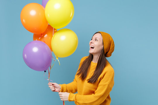 Laughing young woman in sweater and hat posing isolated on blue background. Birthday holiday party people emotions concept. Mock up copy space. Celebrating hold colorful air balloons looking aside.