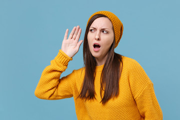 Displeased young brunette woman girl in yellow sweater and hat posing isolated on blue background...