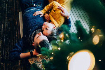 Naklejka na ściany i meble Couple in love embracing on floor under decorated Christmas tree