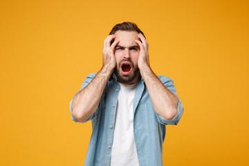 Shocked young bearded man in casual blue shirt posing isolated on yellow orange wall background...