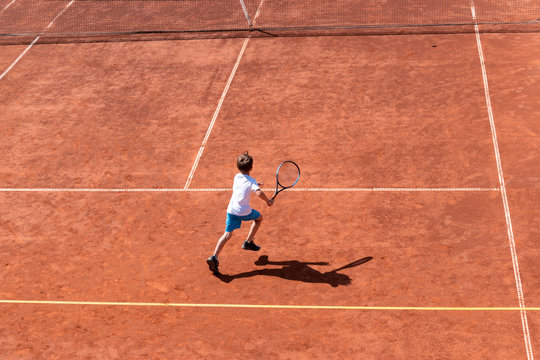 Boy tennis player running on a red clay court for a short ball. Top view, copy space. Training, kids tournament, match