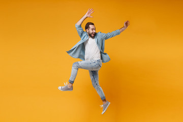 Fototapeta na wymiar Joyful young bearded man in casual blue shirt posing isolated on yellow orange wall background studio portrait. People sincere emotions lifestyle concept. Mock up copy space. Jumping, rising hands up.