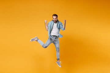 Fototapeta na wymiar Joyful young bearded man in casual blue shirt posing isolated on yellow orange background, studio portrait. People sincere emotions lifestyle concept. Mock up copy space. Jumping doing winner gesture.