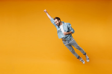 Fototapeta Funny young bearded man in casual blue shirt posing isolated on yellow orange background, studio portrait. People lifestyle concept. Mock up copy space. Jumping with outstretched hand like Superman. obraz