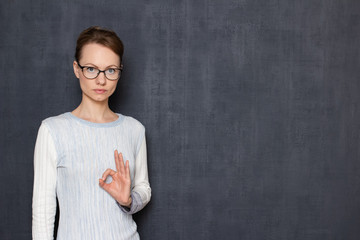 Portrait of serious girl with glasses, showing okay gesture or zero